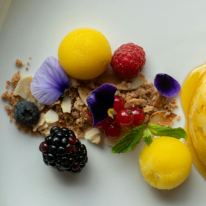 A beautifully plated dessert with mango sorbet, fresh berries, and edible flowers.