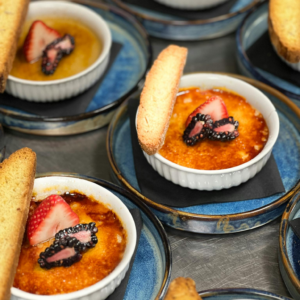 Gourmet creme brulee desserts garnished with fresh berries and biscotti on stylish plates.